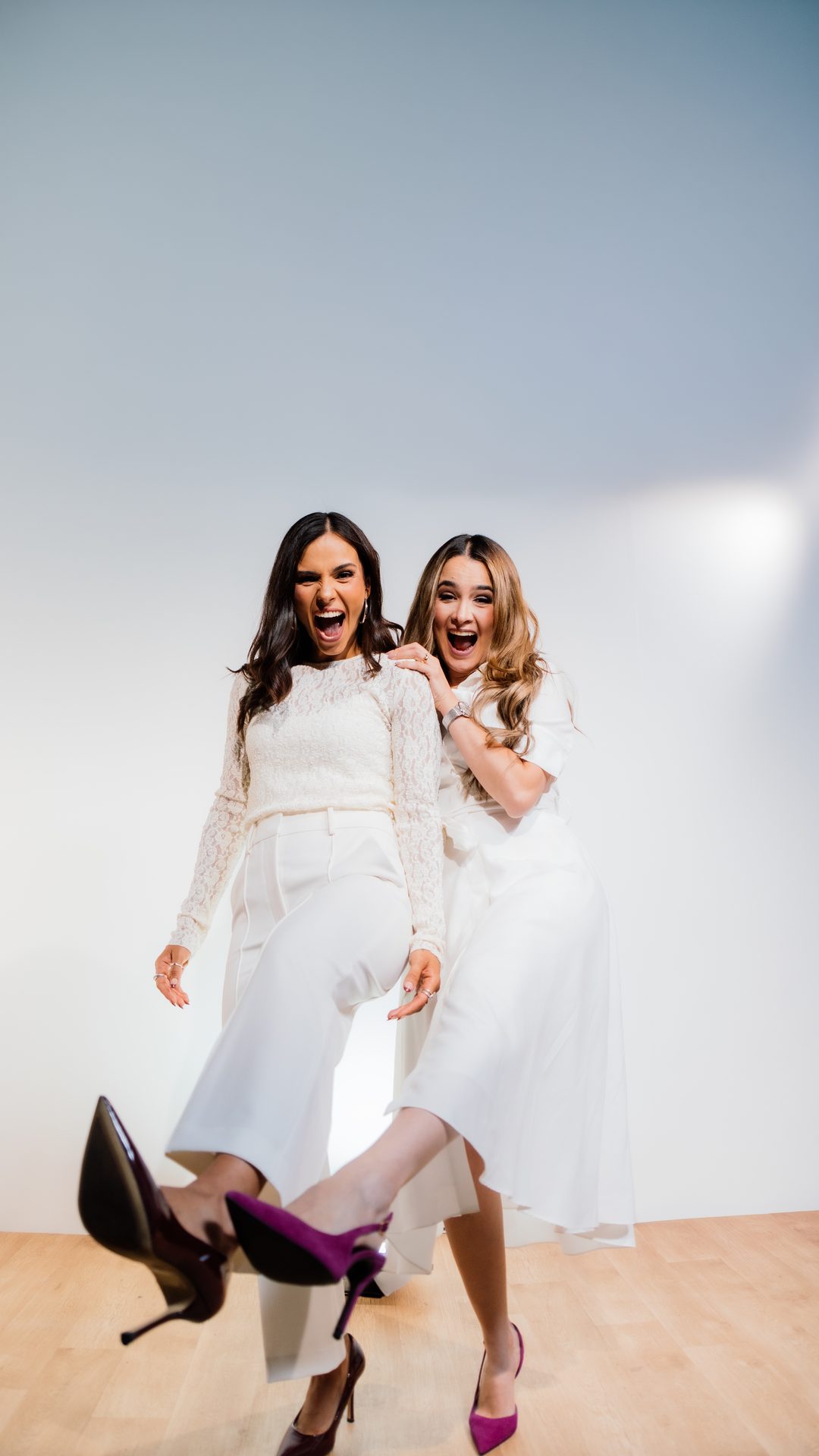 Michelle Ruiz y Ana Fidalgo, vestidas de blanco, de cuerpo entero y riendo en un estudio de fondo claro.
